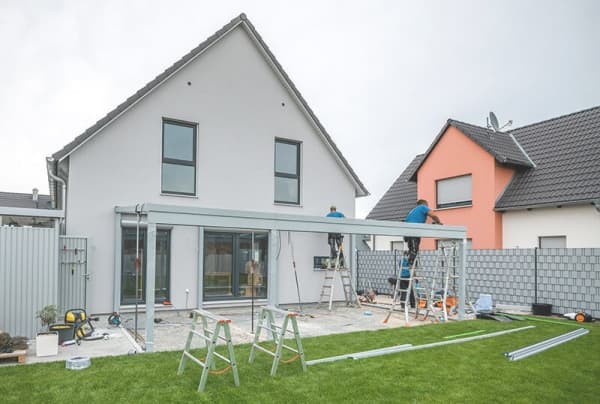 Handwerker installieren eine Terrassenüberdachung an einem modernen Einfamilienhaus mit großem Garten.