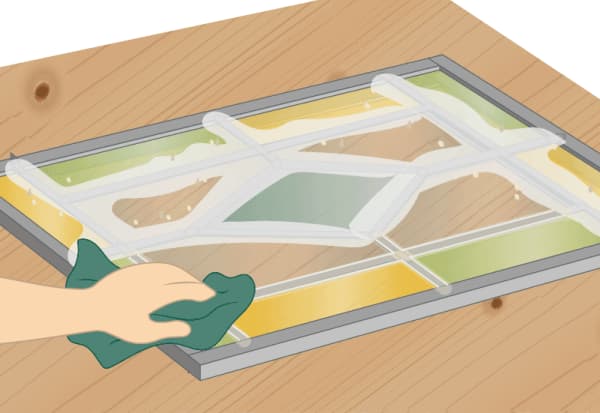 Hand wischt überschüssigen Kitt von Bleiglasfenster auf Holztisch ab