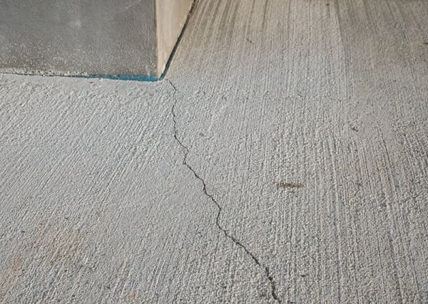Betonriss im Betonboden, der sich zur Kante einer Wand zieht