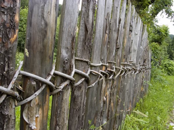 Naturzaun aus dünnen, unregelmäßigen Latten, die vertikal angeordnet und mit geflochtenen Ruten verbunden sind