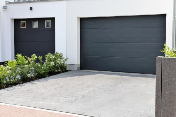 Gemauerte weiße Garage mit modernem, grauen Garagentor