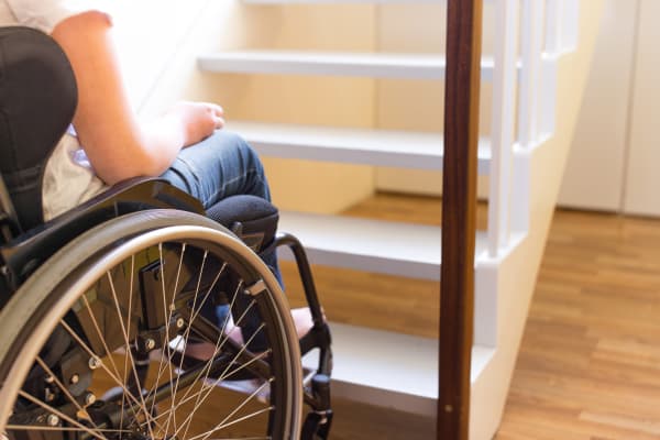 Nahaufnahme einer Person im Rollstuhl am Fuß einer Treppe von hinten