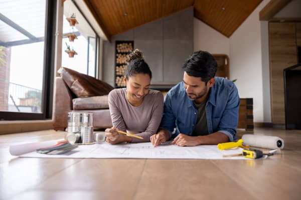 Ein Mann und eine Frau schauen gemeinsam auf dem Boden liegend auf einen Bauplan.