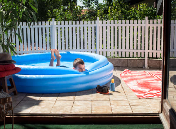 Kind liegt im Pool im Garten auf einer Terrasse mit Fliesen aus Steinfeinzeug