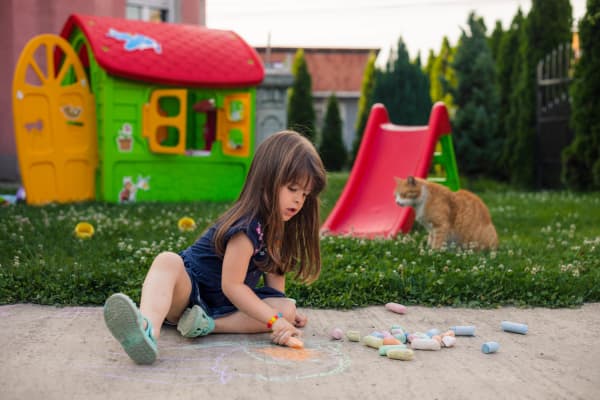 Kind malt mit Kreide auf dem Boden im Garten.