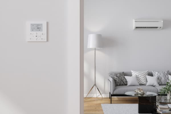 Modernes, hell eingerichtetes Wohnzimmer mit Klimaanlage über dem Sofa und Bedienpanel für Smart Home an der Wand