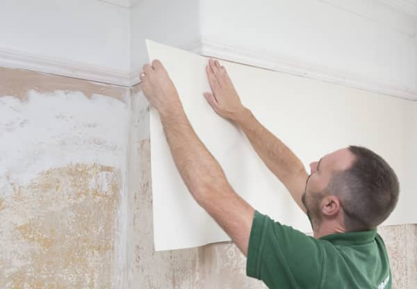 Mann bringt weiße Tapete an die Wand an.