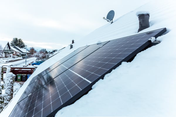 Seitliche Ansicht von Solarmodulen auf einem verschneiten Hausdach im Winter