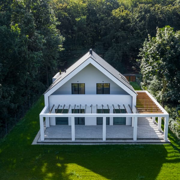 Modernes Haus mit einer L-förmigen Pergola umgeben von hohen Bäumen