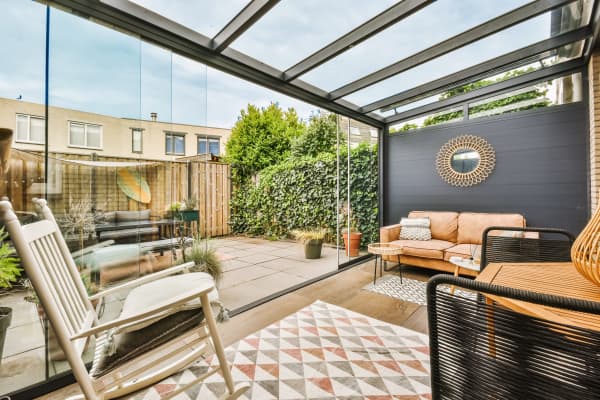 Terrassenüberdachung aus Aluminium mit aufschiebbaren Glaswänden und einer festen Seitenwand.