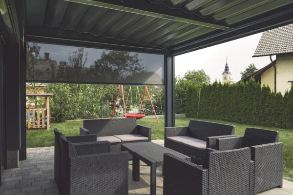 Terrassenüberdachung mit Sitzgruppe und einem halb heruntergefahrenen Seitenrollo