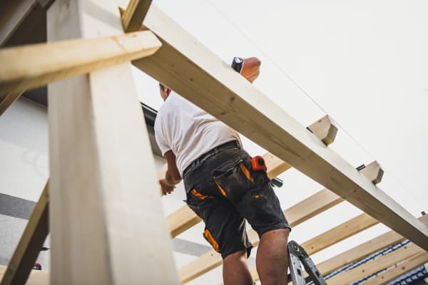 Arbeiter legt Sparren auf Fußpfette beim Bau einer Terrassenüberdachung.