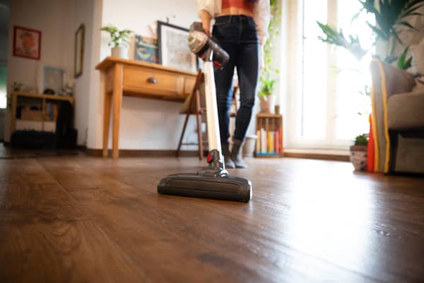 Frau saugt das Wohnzimmer mit einem kabellosen Staubsauger