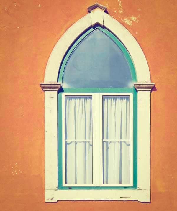 Spitzbogenfenster mit weißem Rahmen und Vorhängen an orangefarbener Fassade