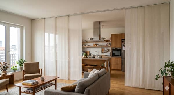 Wohnbereich mit Sofa und offener Küche hinter halbtransparenten Schiebegardinen