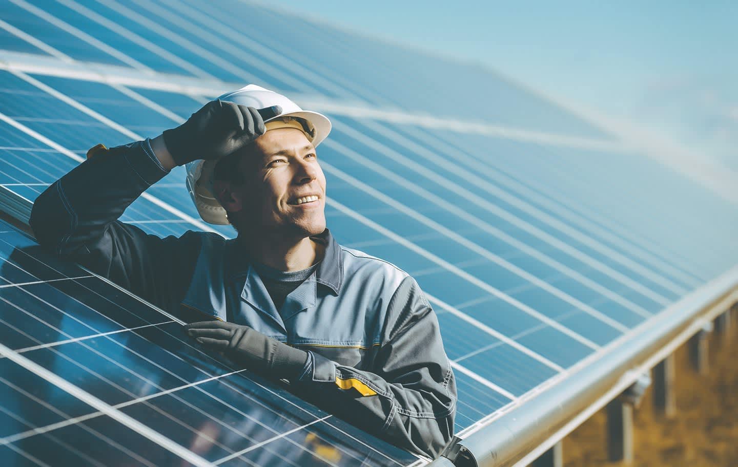 Bauarbeiter steht zwischen blauen Solarpaneels und guckt in den blauen Himmel