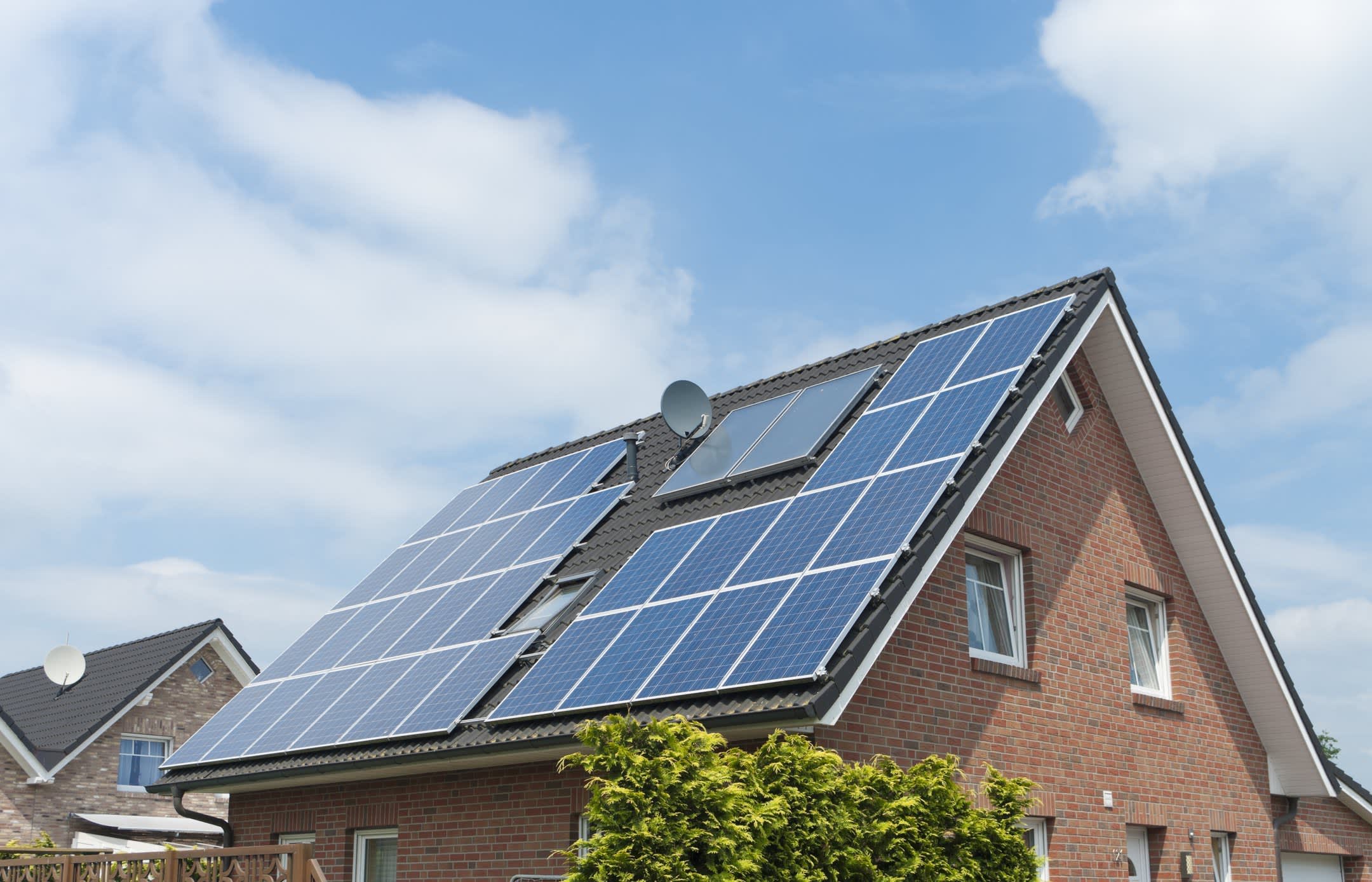 Einfamilienhaus aus rotem Backstein mit großer Photovoltaikanlage auf dem Dach vor blauem Himmel und weißen Wolken