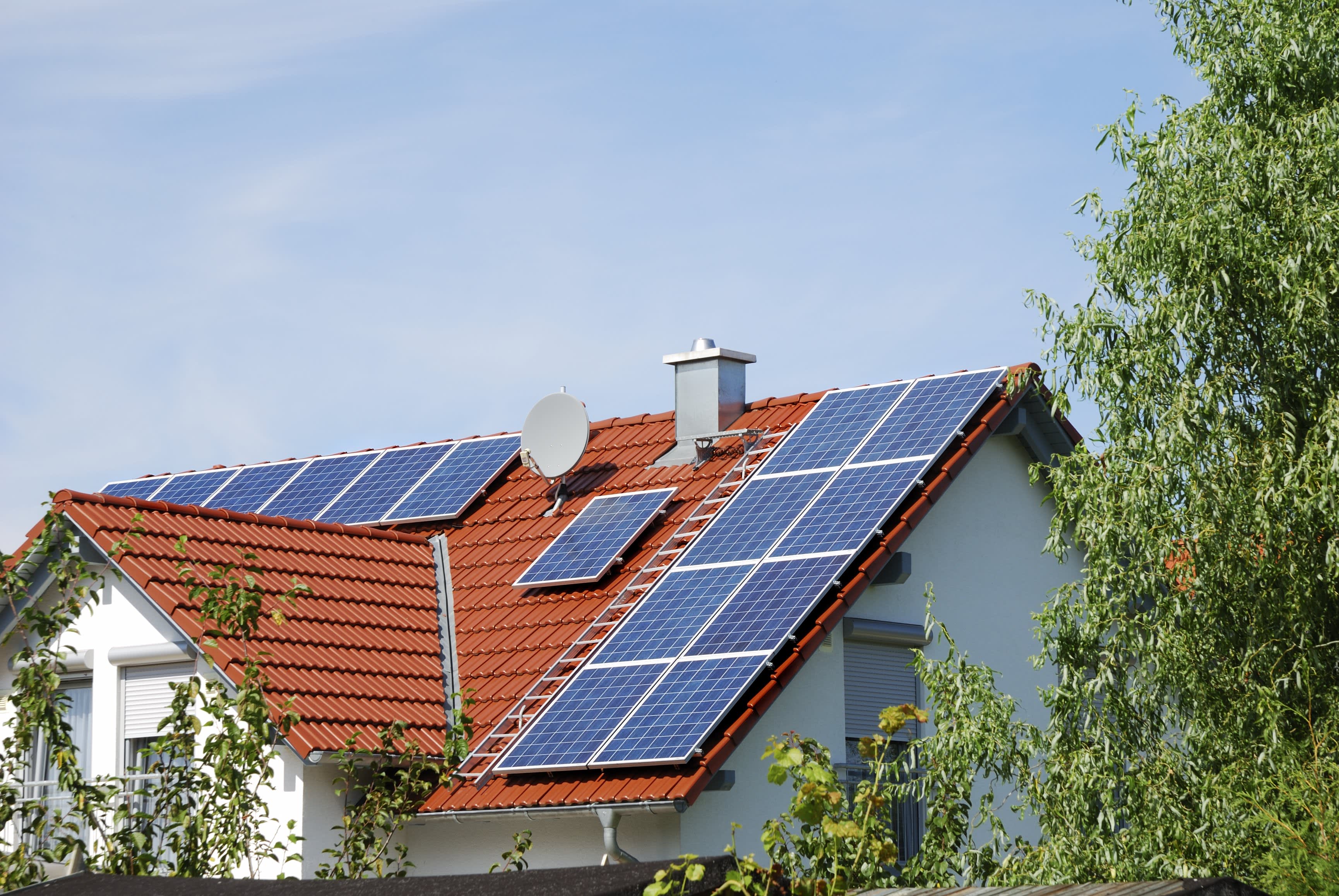 Einfamilienhaus mit Solaranlage auf rotem Ziegeldach vor blauem Himmel