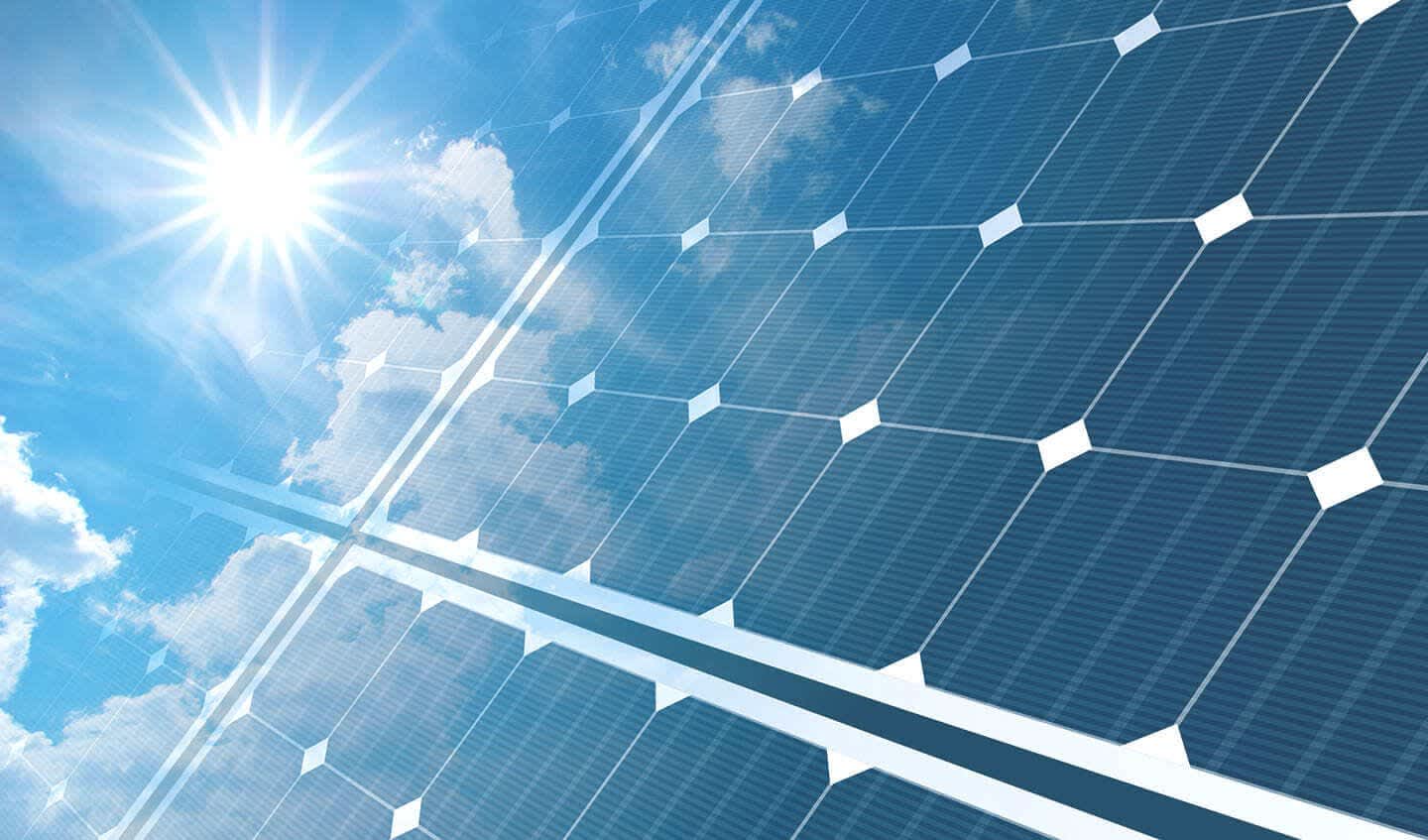 Photovoltaikmodule auf einem Schrägdach, auf die die Sonne bei blauem, leicht bewölktem Himmel scheint