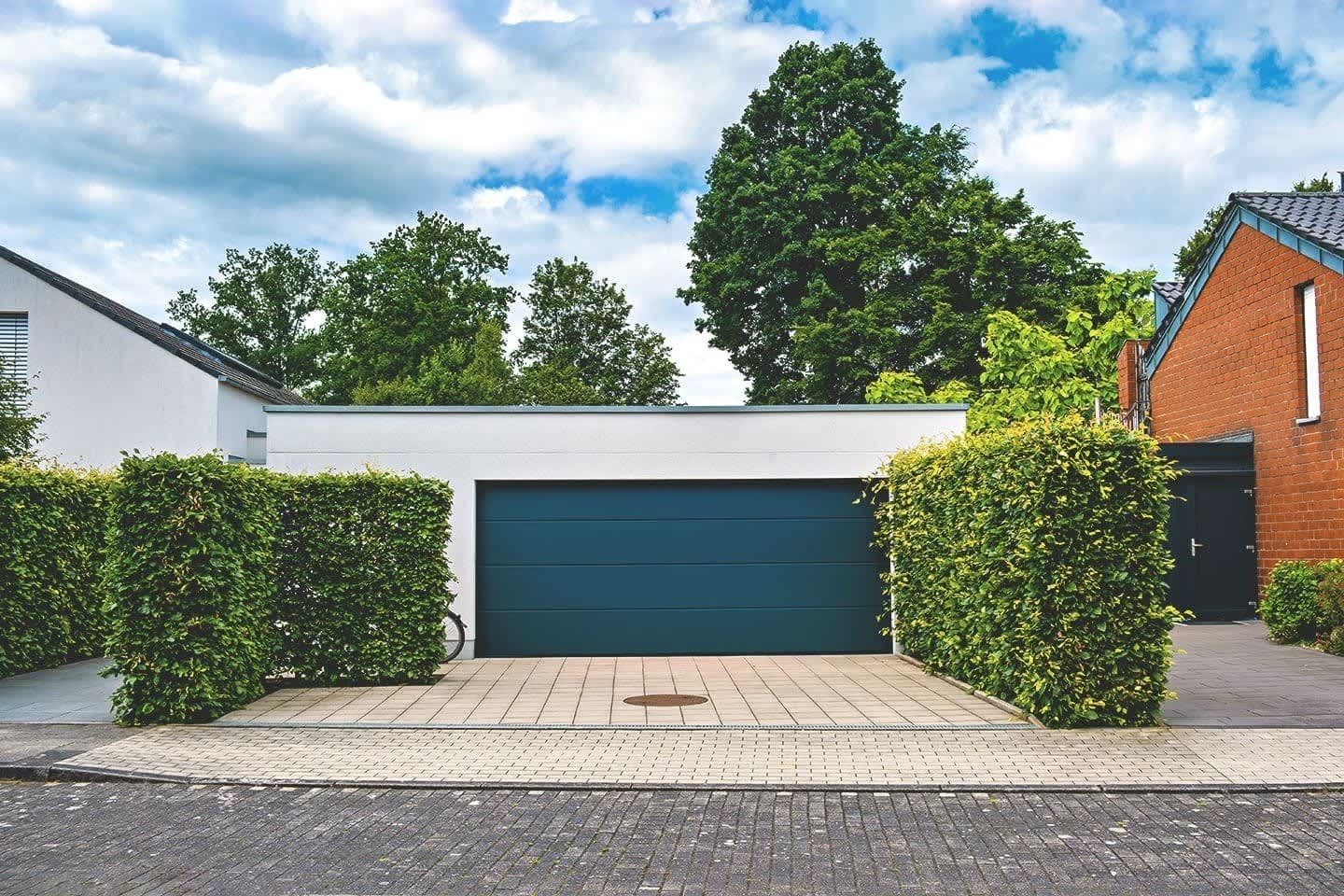 Großraumgarage aus Beton mit Hecken neben Wohnhaus