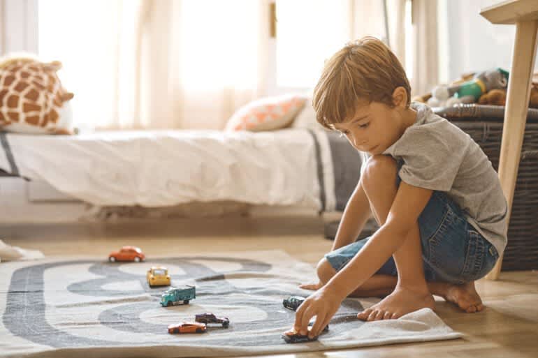 Kind spielt auf dem Fußboden im Kinderzimmer mit Autos