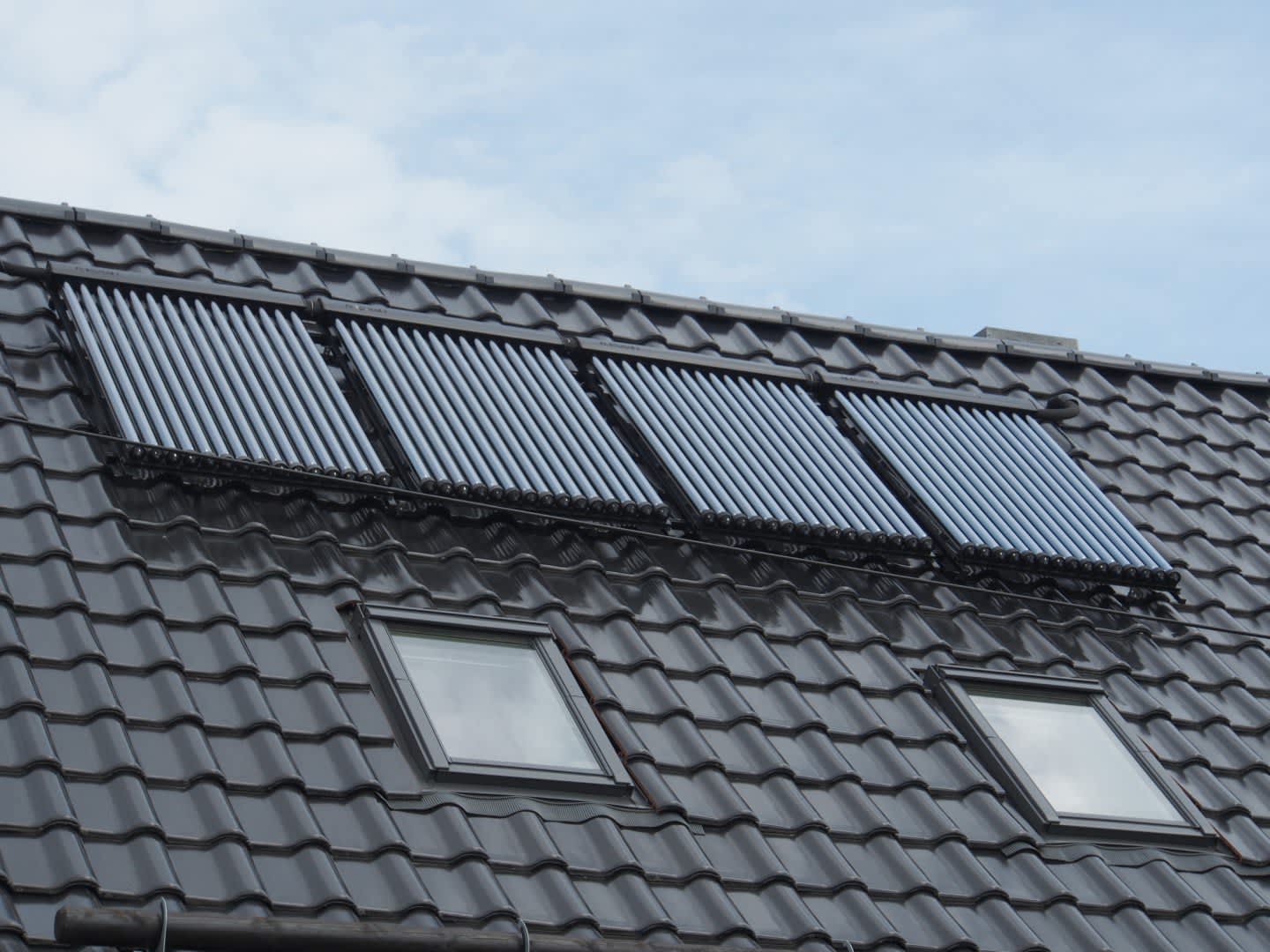 Solarkollektoren auf einem grauen Hausdach mit zwei Dachfenstern