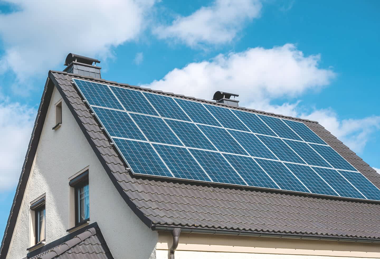 Einfamilienhaus mit Solaranlage auf grauem Dach vor blauem Himmel mit weißen Wolken