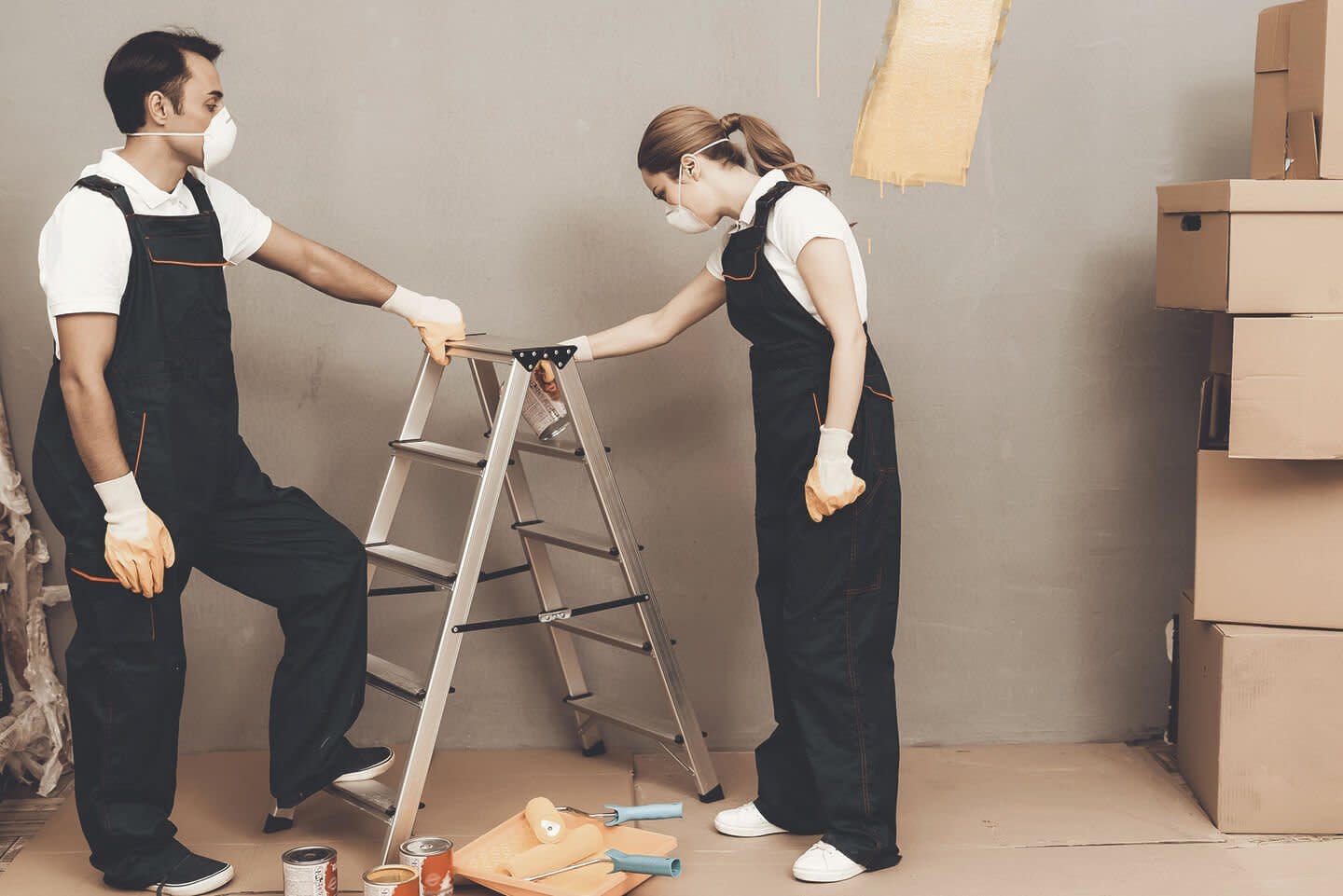 Mann und Frau stehen an einer Leiter und streichen eine Wand, dabei tragen sie Masken.