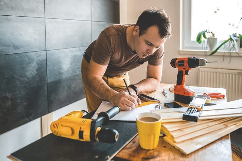 Handwerker beugt sich mit Stift in der Hand über einen Tisch