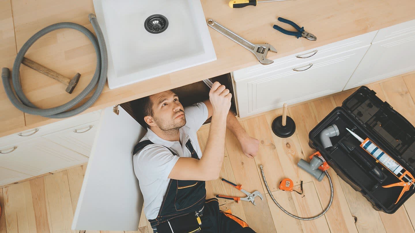 Handwerker führt Reparaturen unter einer Spüle durch und liegt dabei auf dem Boden