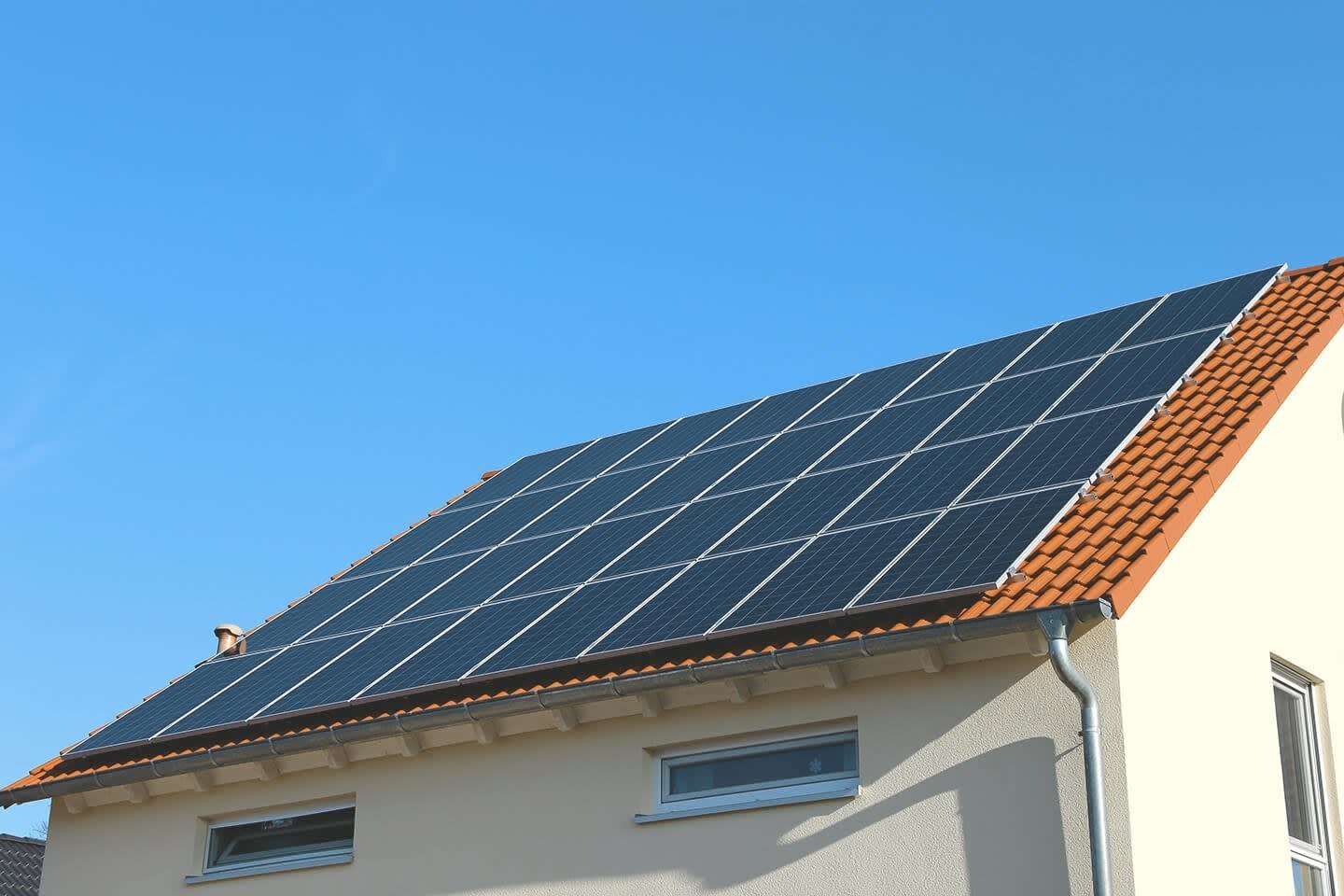 Hausdach mit einer großen Solaranlage aus blauen Modulen darauf.