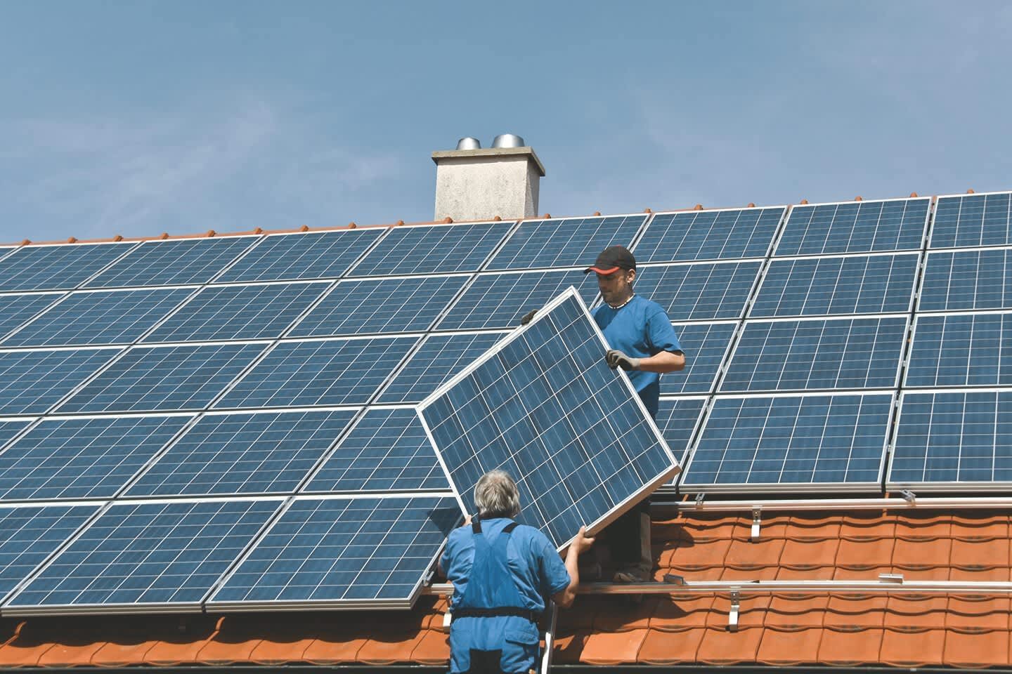 Handwerker decken Dach mit Solaranlage ein.