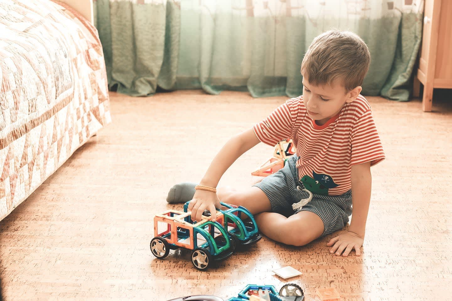 Junge spielt mit Spielzeugauto auf Korkboden im Zimmer