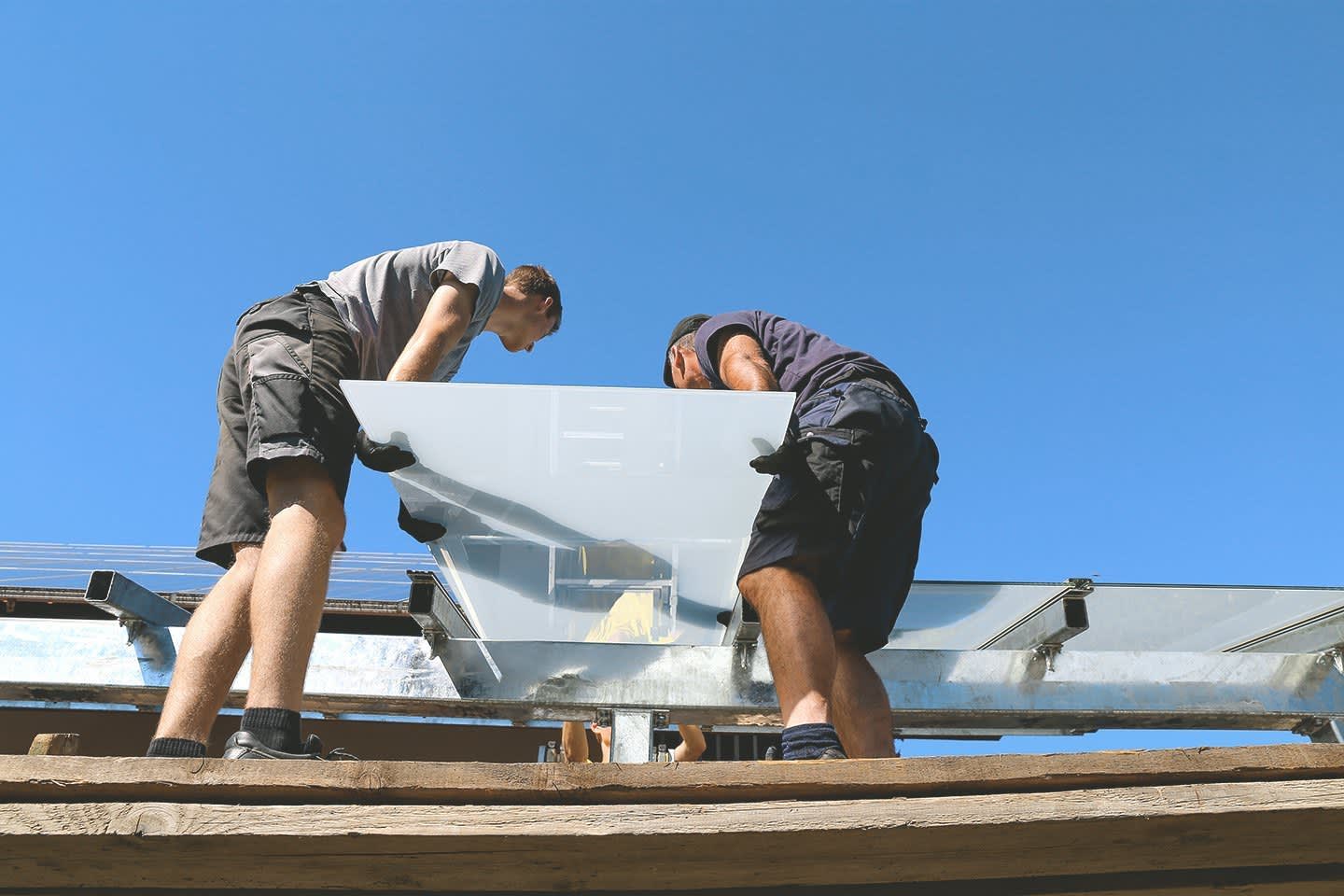 Zwei Handwerker installieren eine Glas-Terrassenüberdachung.