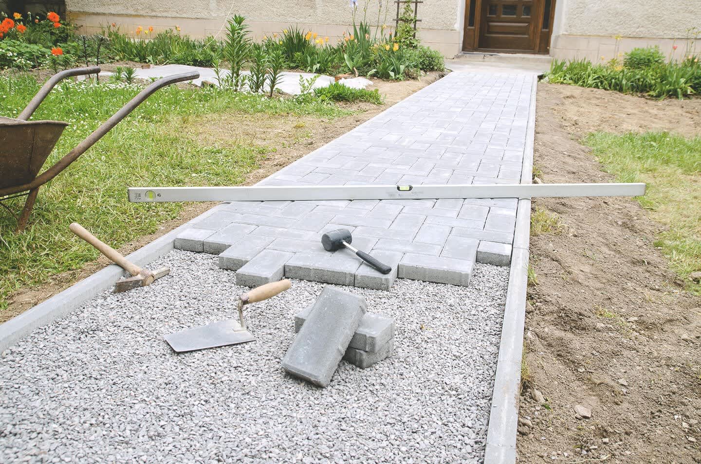 Teilweise fertig verlegter Gartenweg mit Wasserwaage und Werkzeugen im Garten