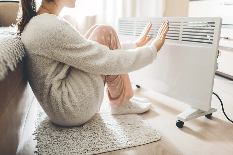 Frau sitzt vor Elektroheizung