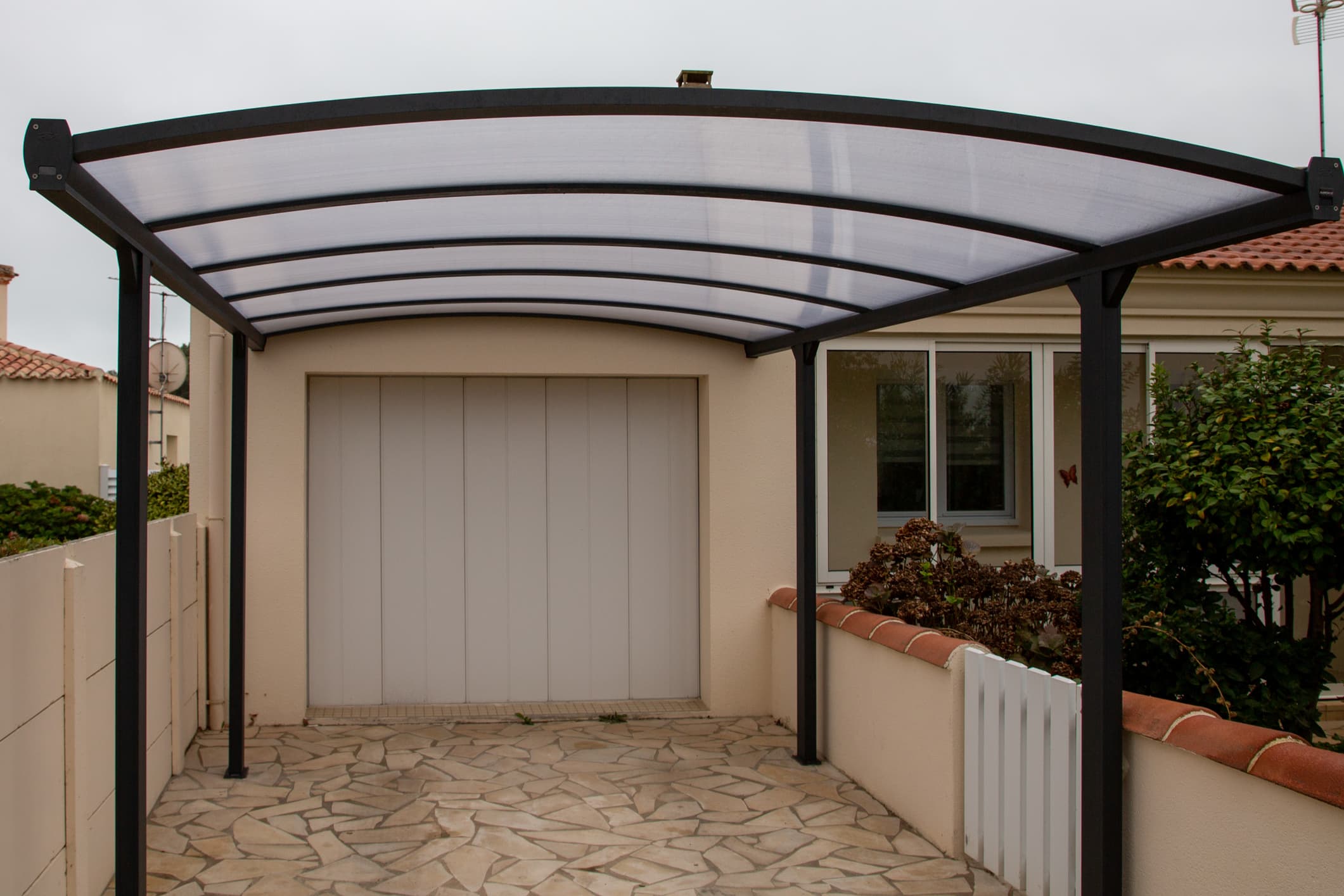 Carport vor einer Einzelgarage neben einem Wohnhaus