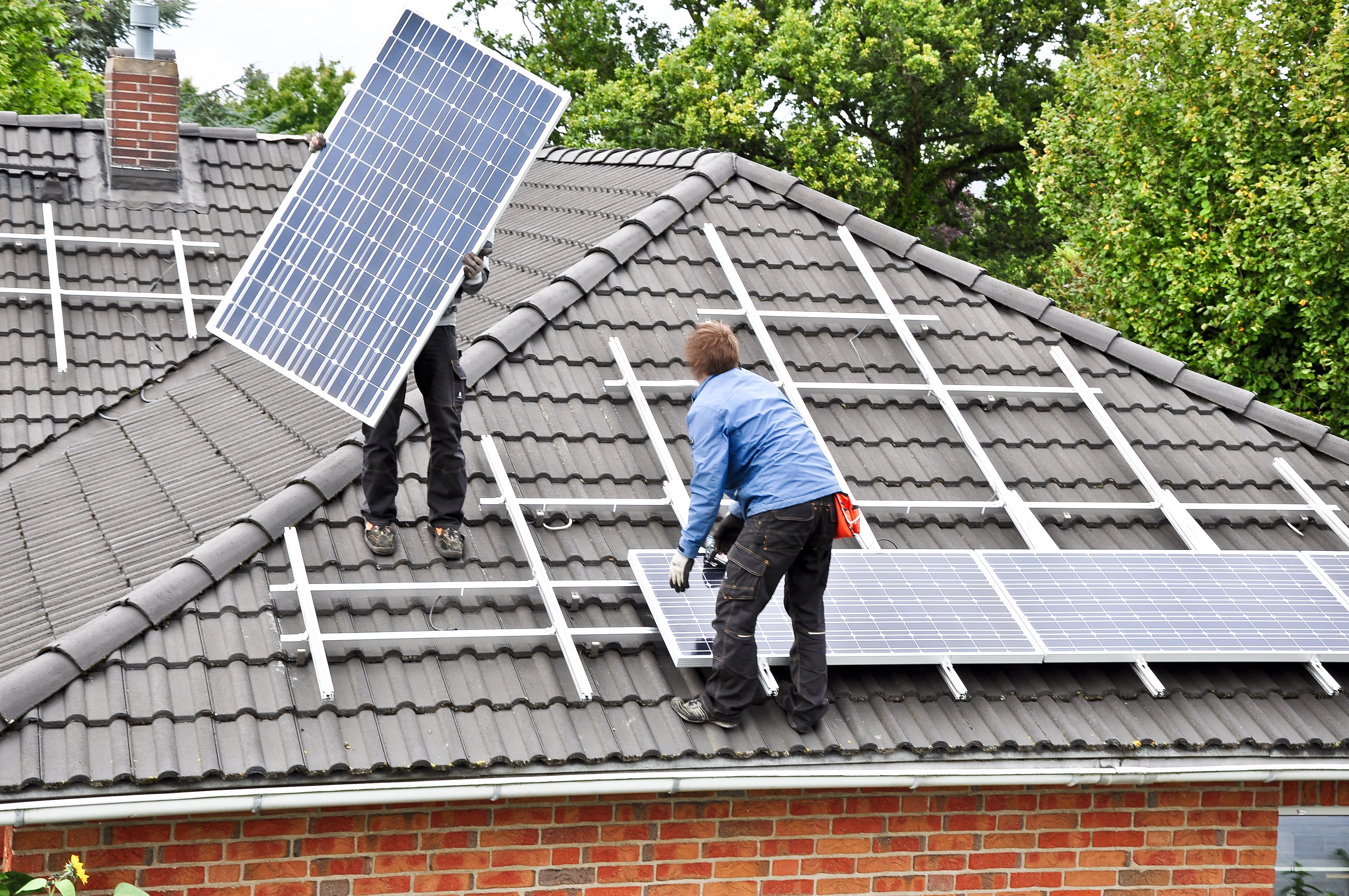 Handwerker montieren zwei Solarpanels auf ein Hausdach