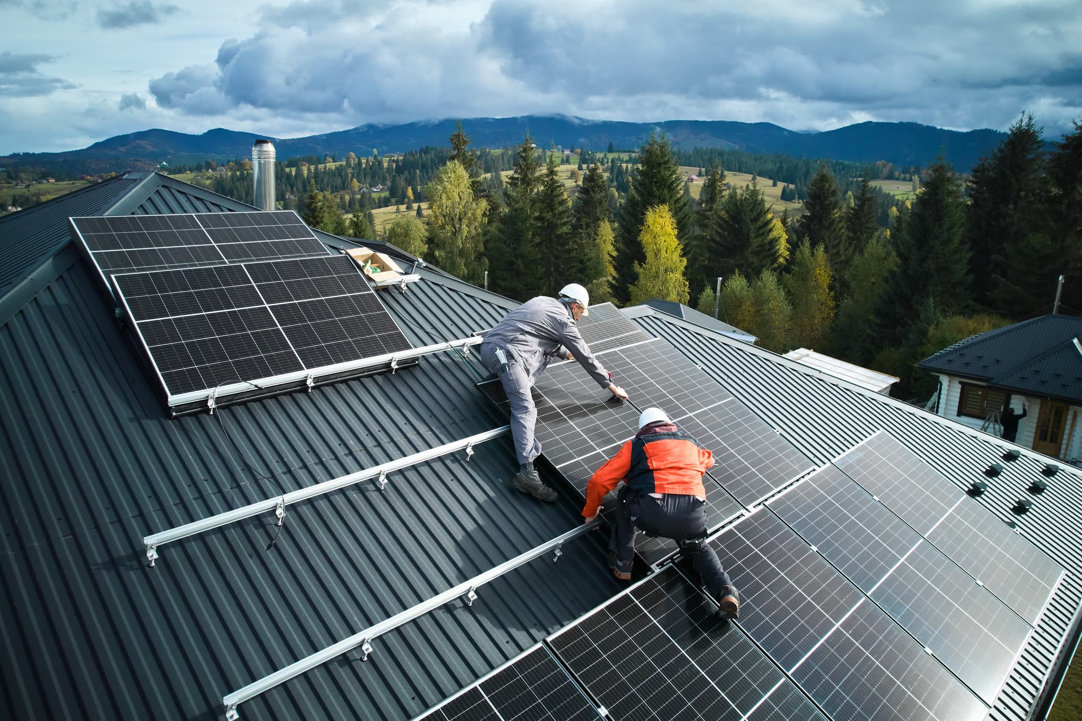 Zwei Installateure errichten eine Solaranlage auf einem Wohnhaus vor schöner Waldkulisse