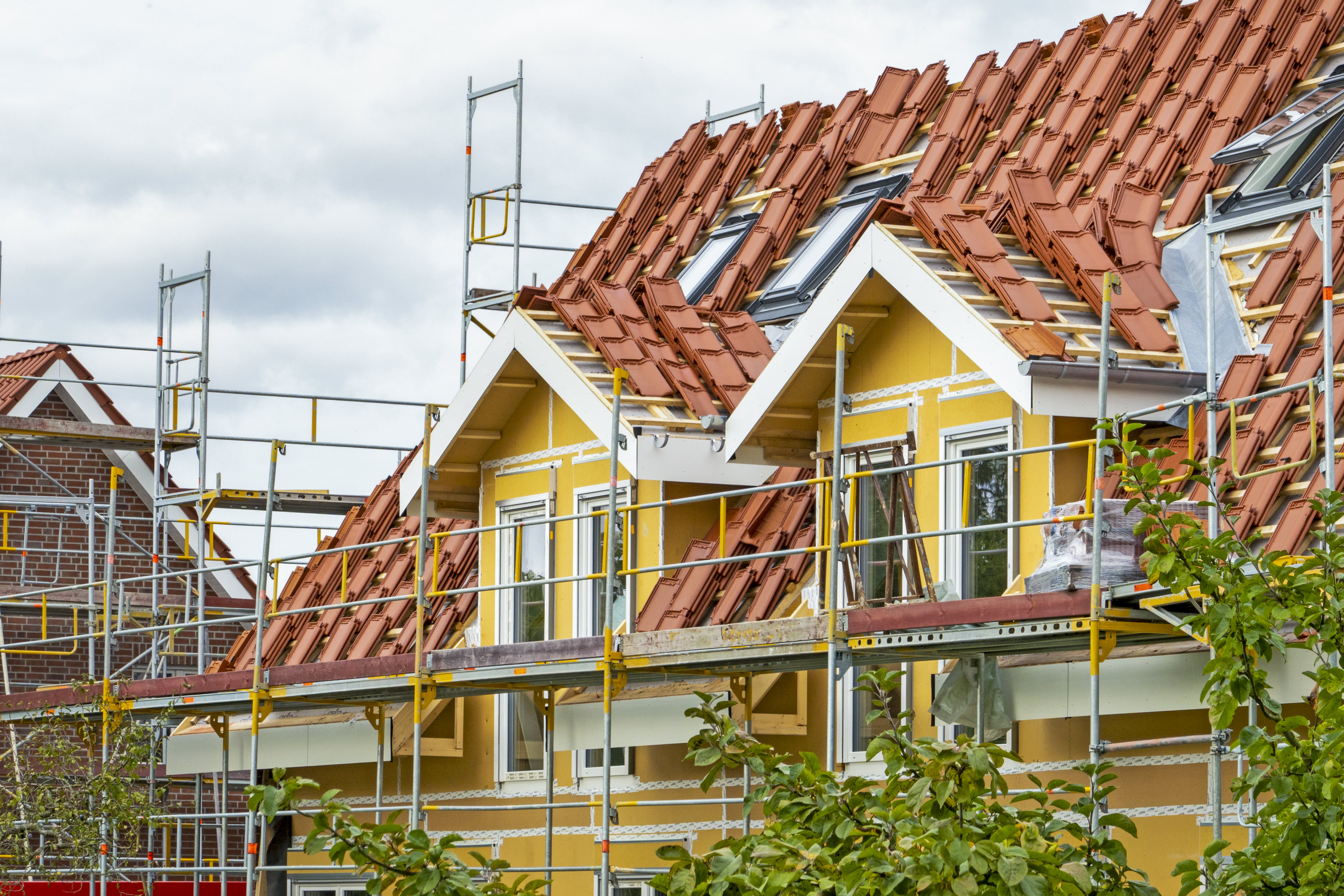 Gerüst an Wohnhaus mit gelber Fassade, dessen Dach neu gedeckt werden soll