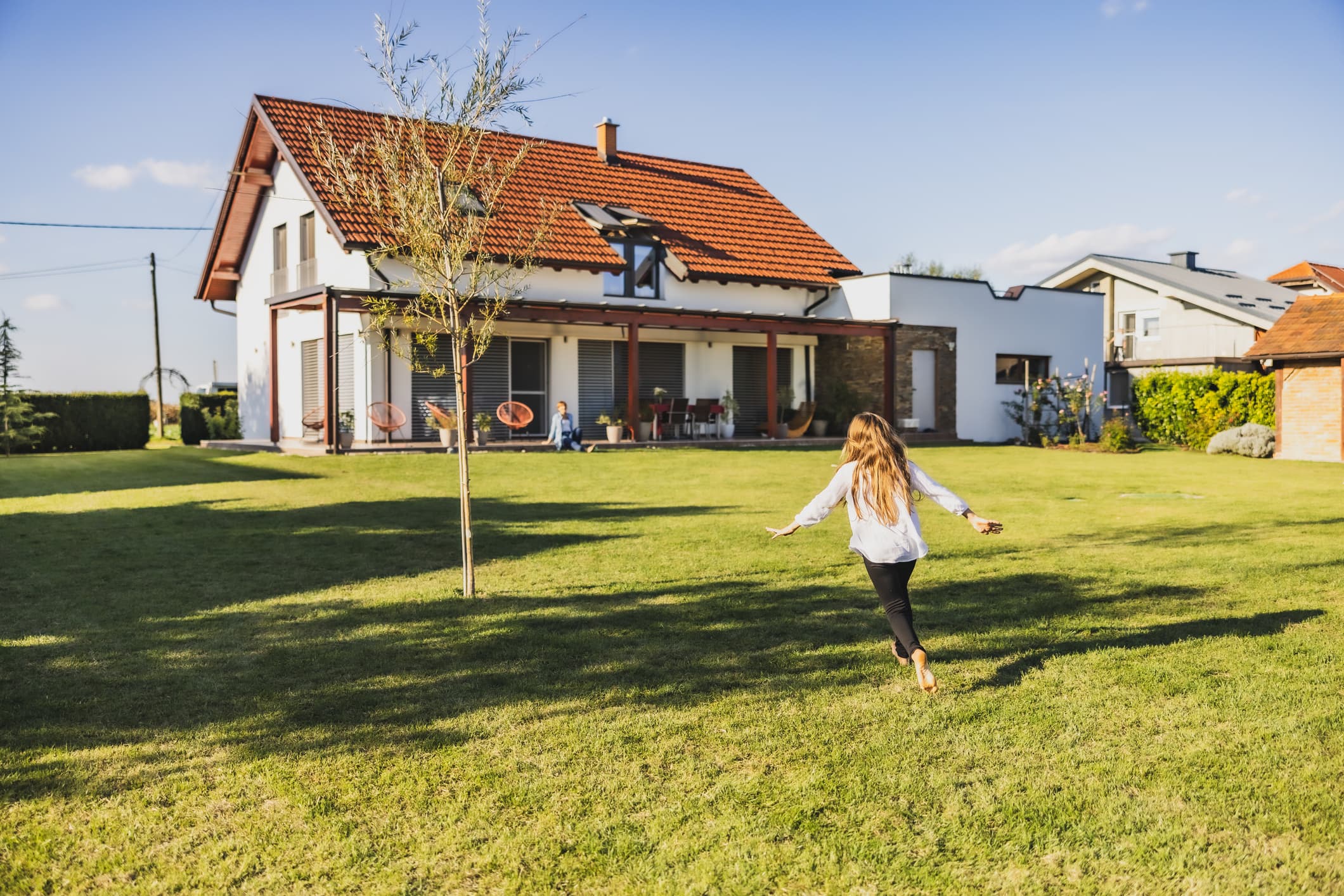 Mädchen rennt mit ausgebreiteten Armen durch den Garten aufs Wohnhaus zu