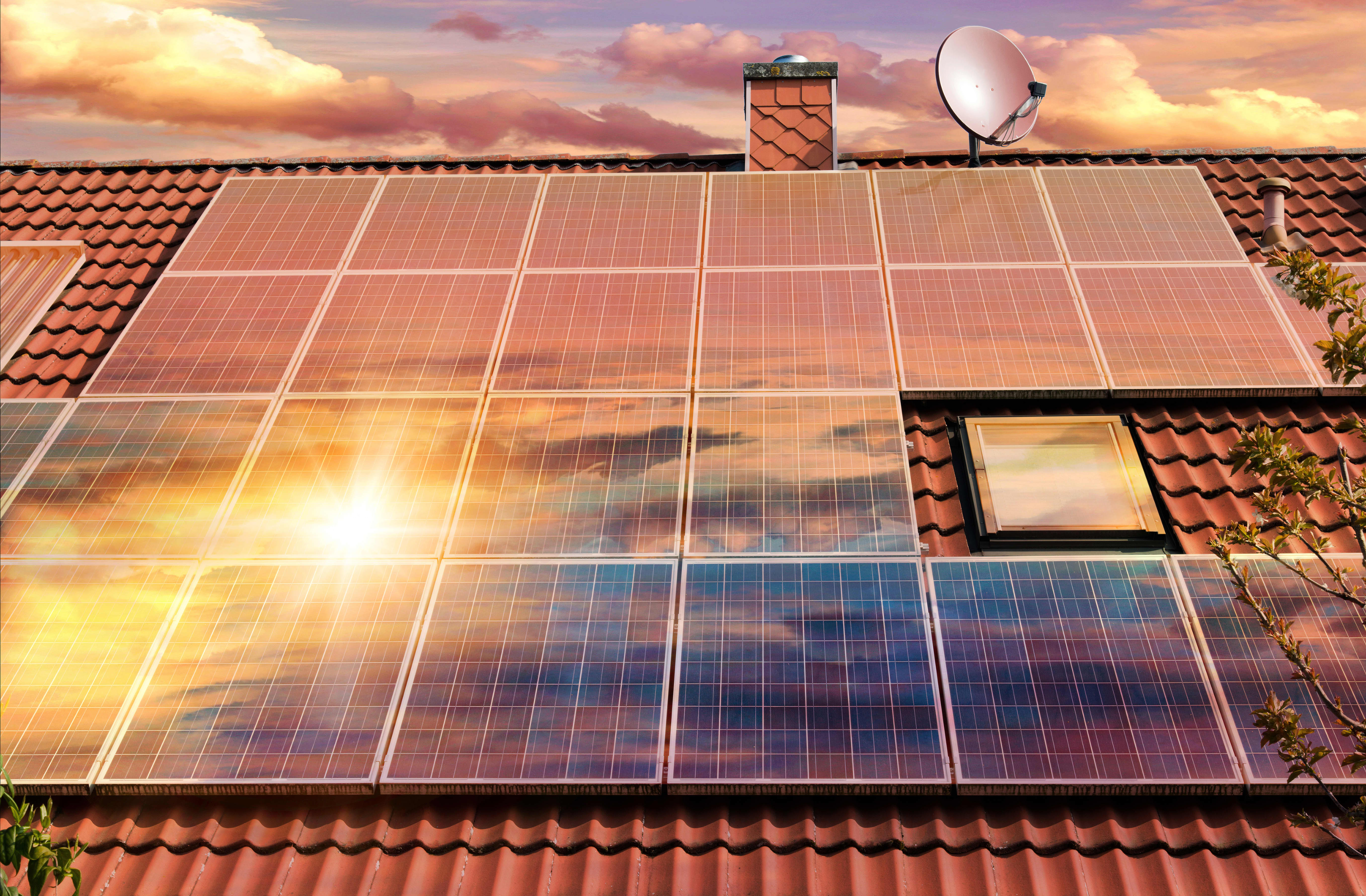 Solarmodule auf dem rot gedeckten Dach eines Hauses und Himmel mit untergehender Sonne