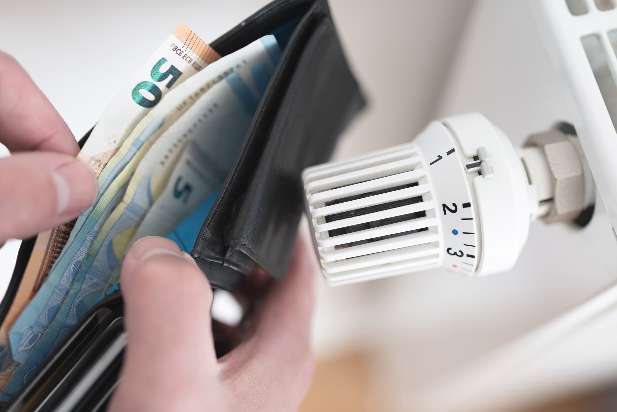 Nahaufnahme einer Geldbörse mit Bargeld neben Thermostat am Heizkörper