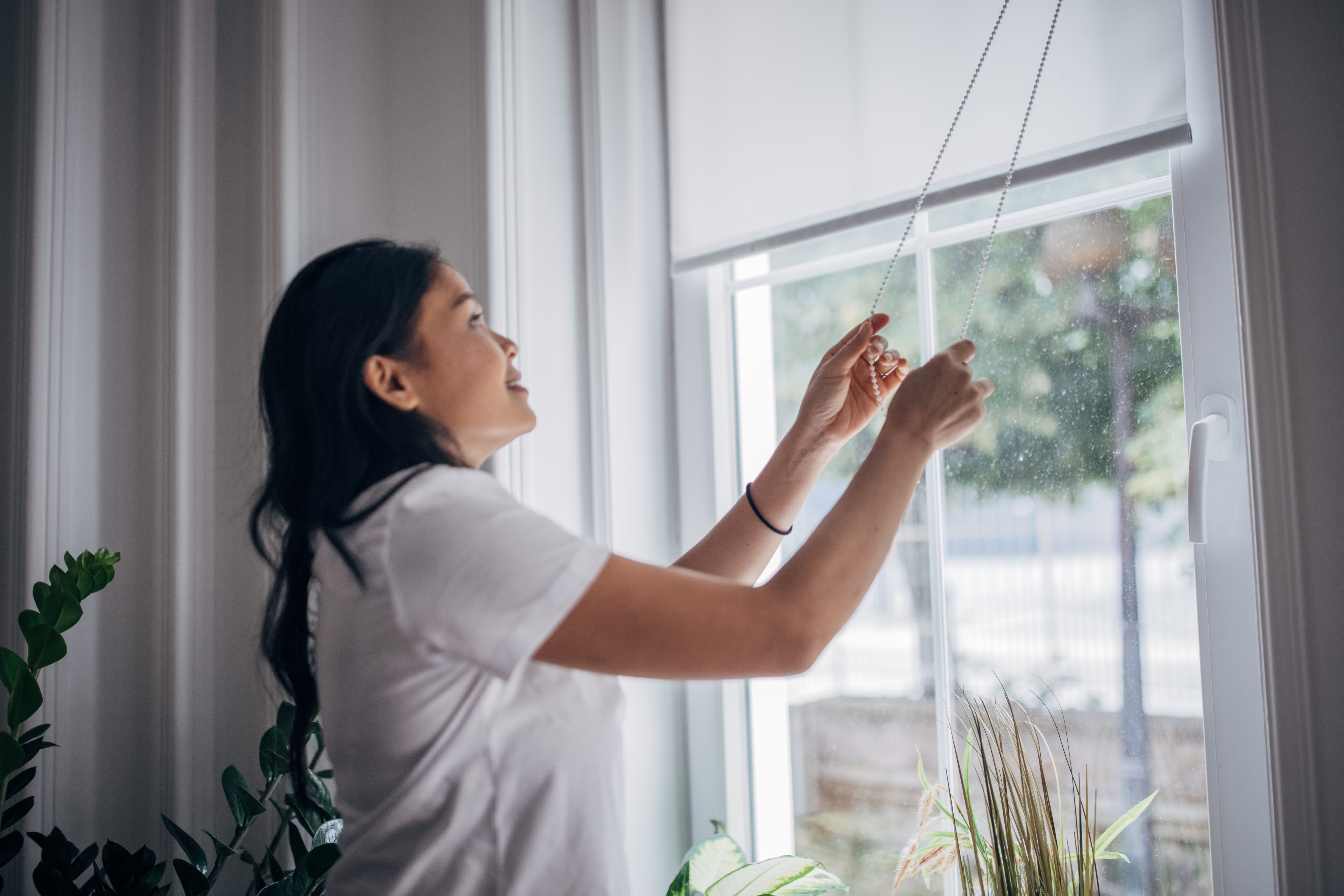 Frau bedient Fensterrollo mit Kettenzug im modernen Wohnraum