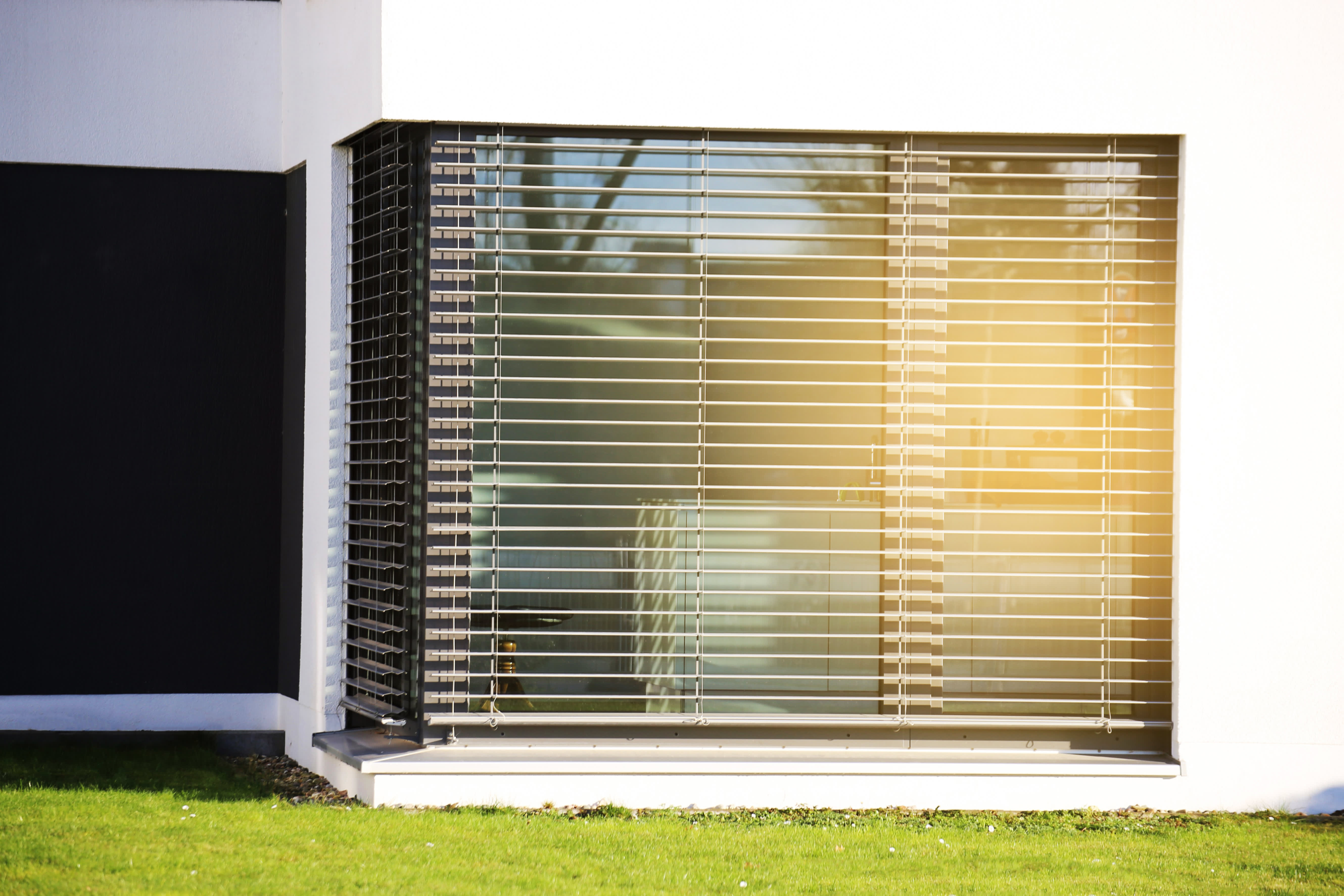 Bodentiefe Fenster mit halboffenen Jalousien, auf die die Sonne scheint