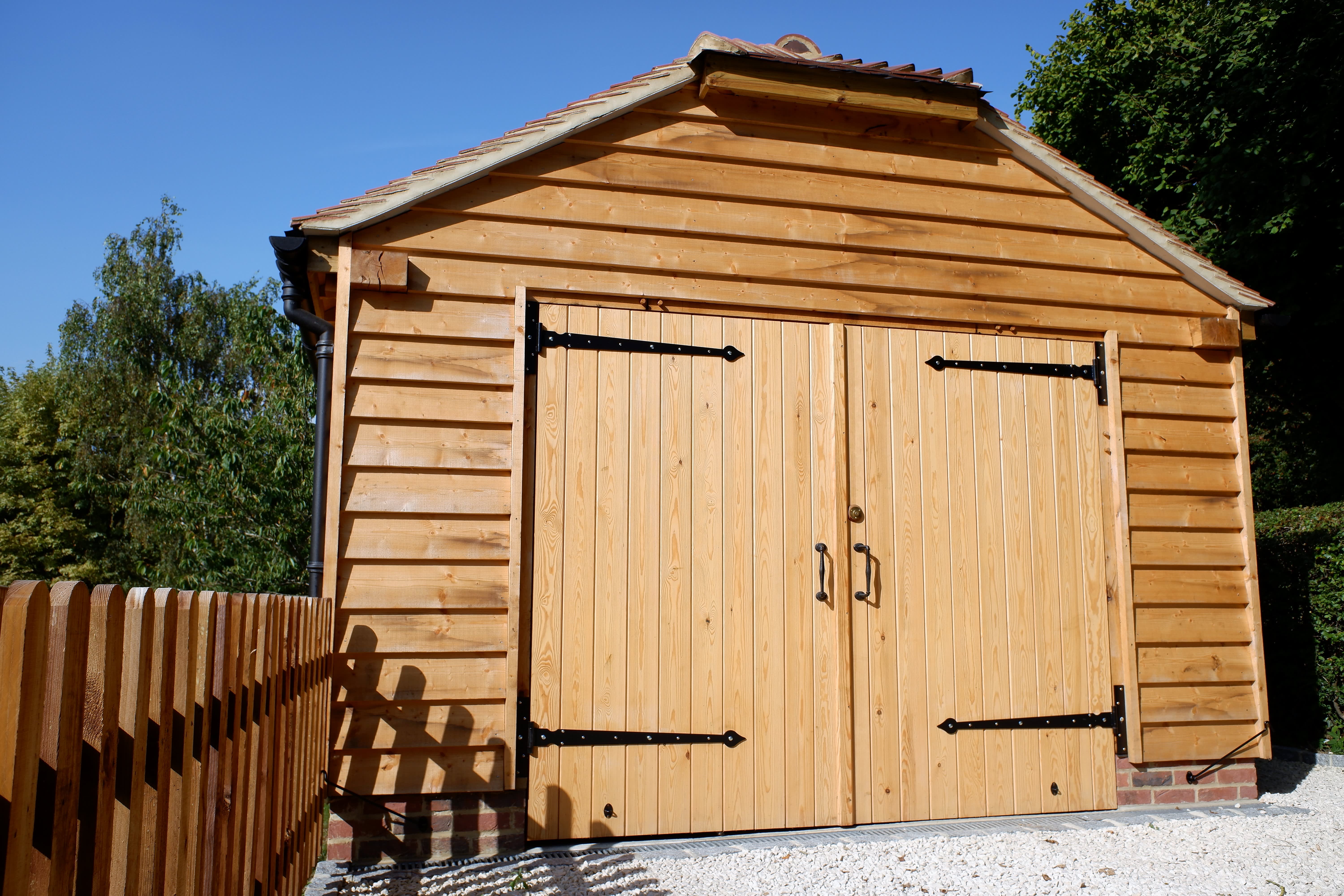 Eine einfache Holzgarage aus unbehandeltem Holz mit einem Flügeltor auf einem privaten Grundstück.