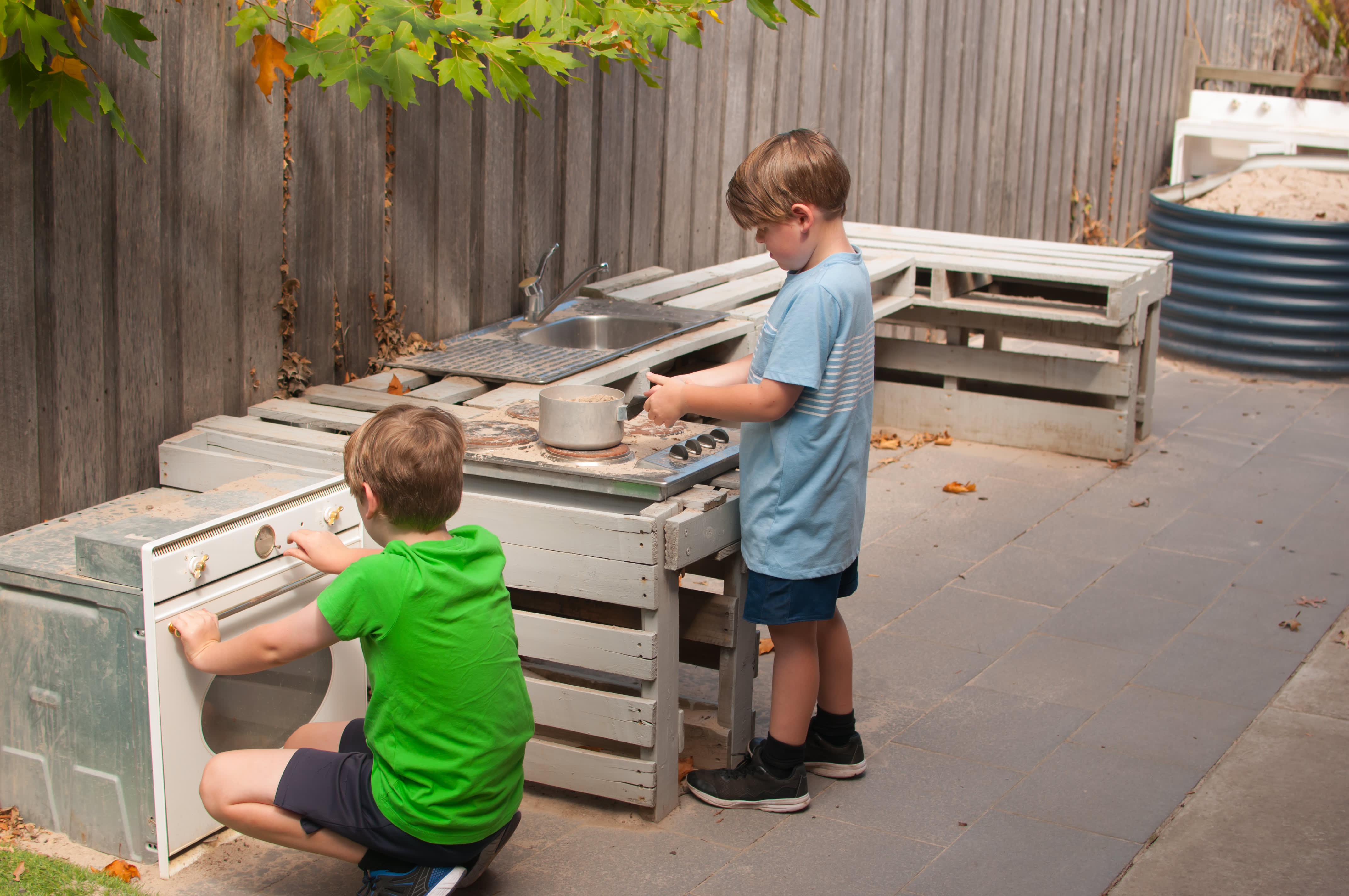 Zwei Jungs spielen in einer Matschküche im Garten.