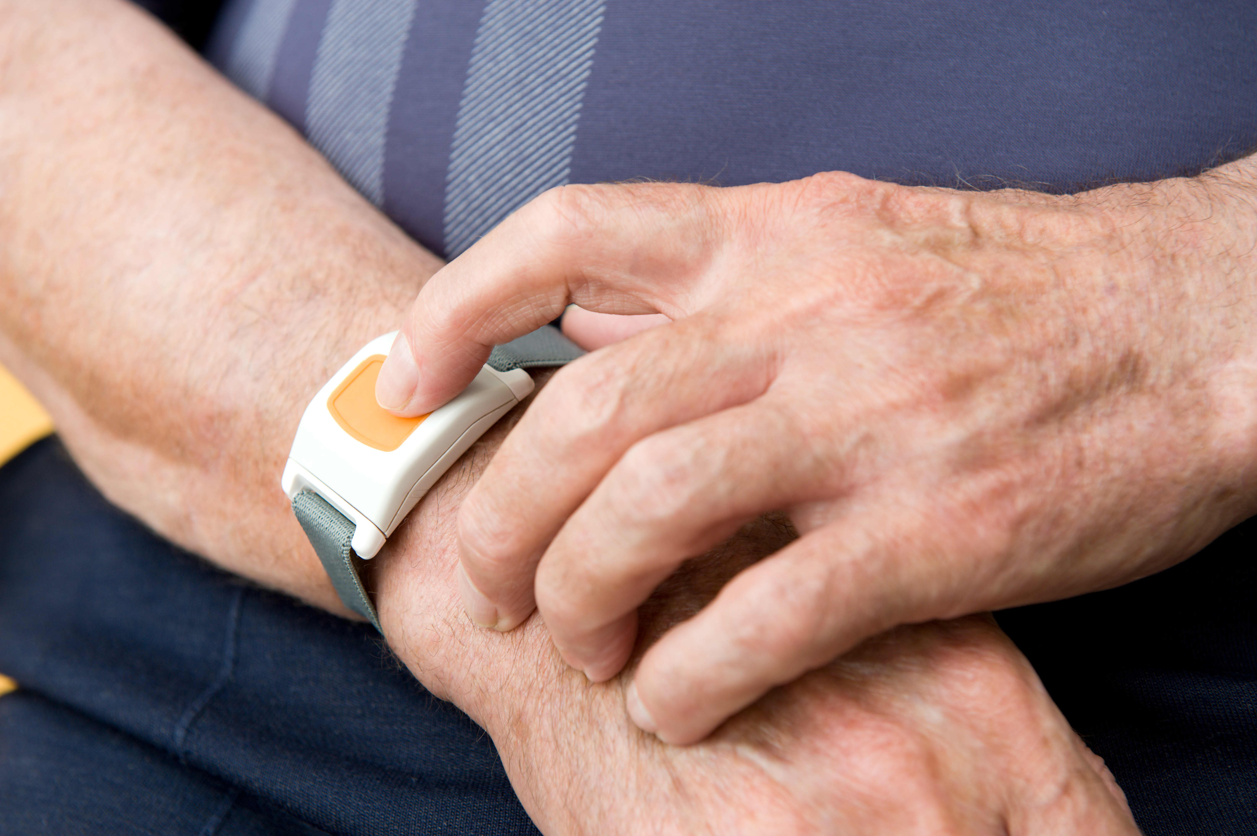 Mann in blauem T-Shirt drückt gelben Notrufknopf an einem Armband.