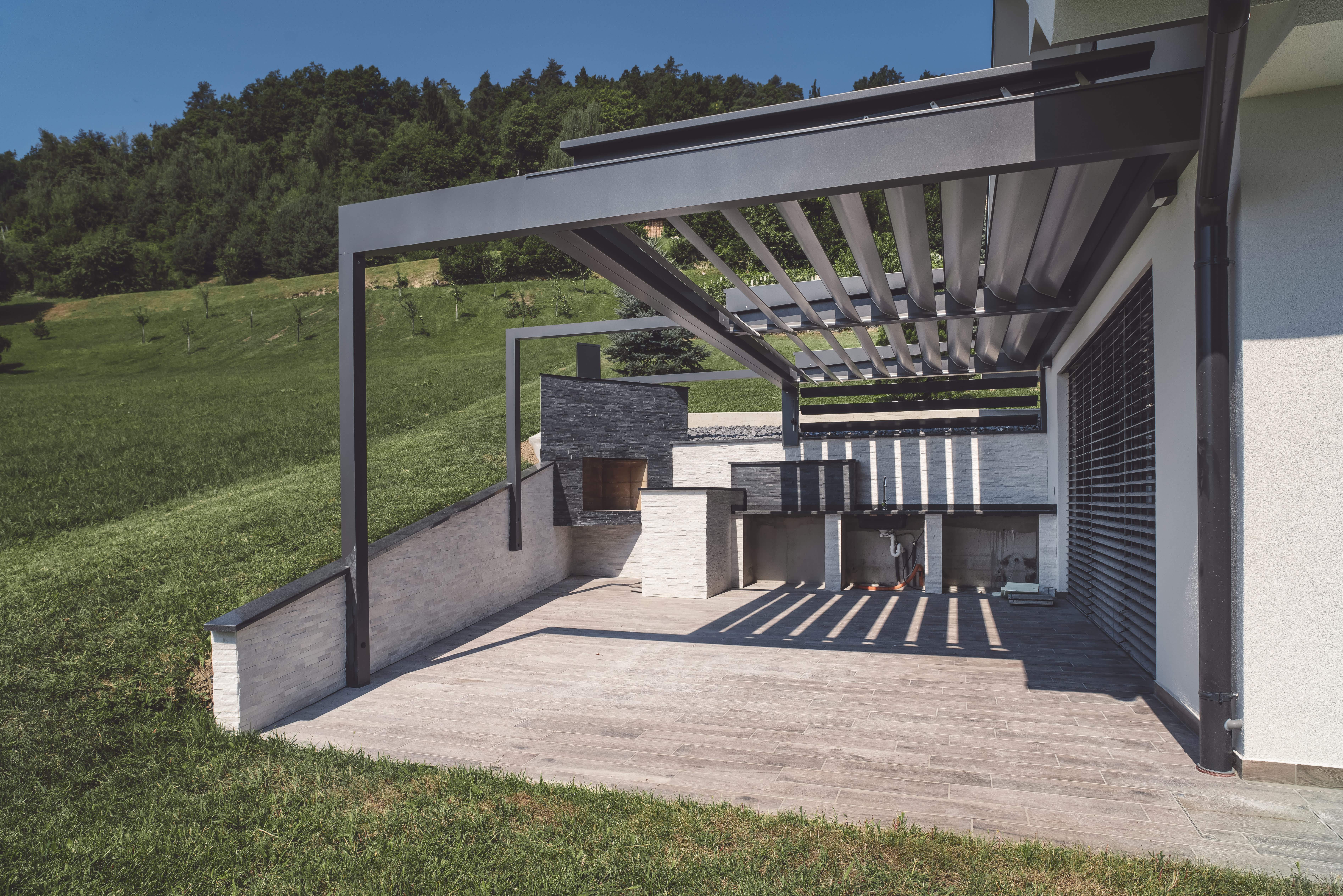 Terrassenüberdachung aus Aluminium mit Lamellendach, am grünen Hang gebaut.