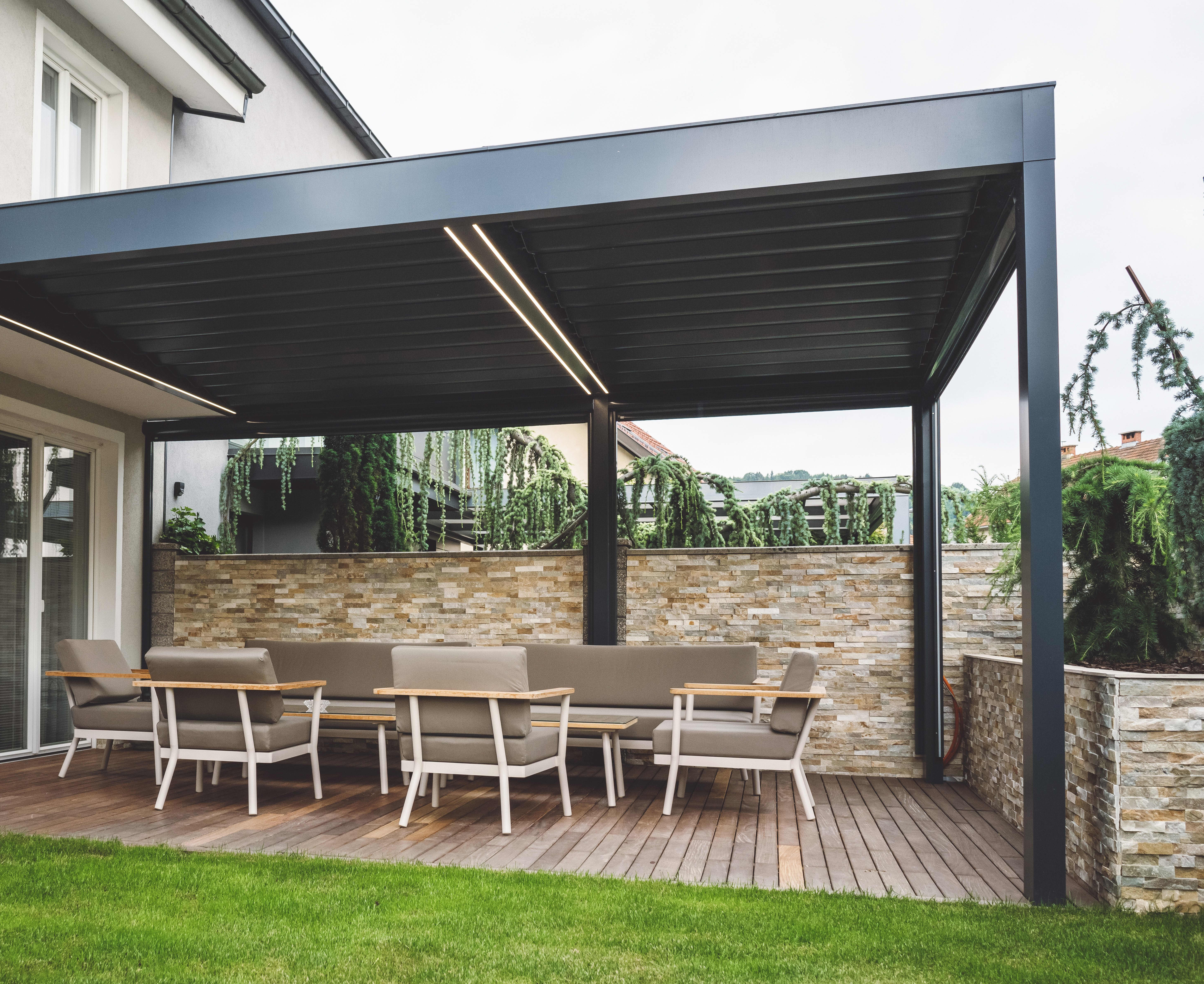 Ans Wohnhaus angebaute schwarze Terrassenüberdachung mit Beleuchtung ist über gemütlichen Loungemöbeln platziert.